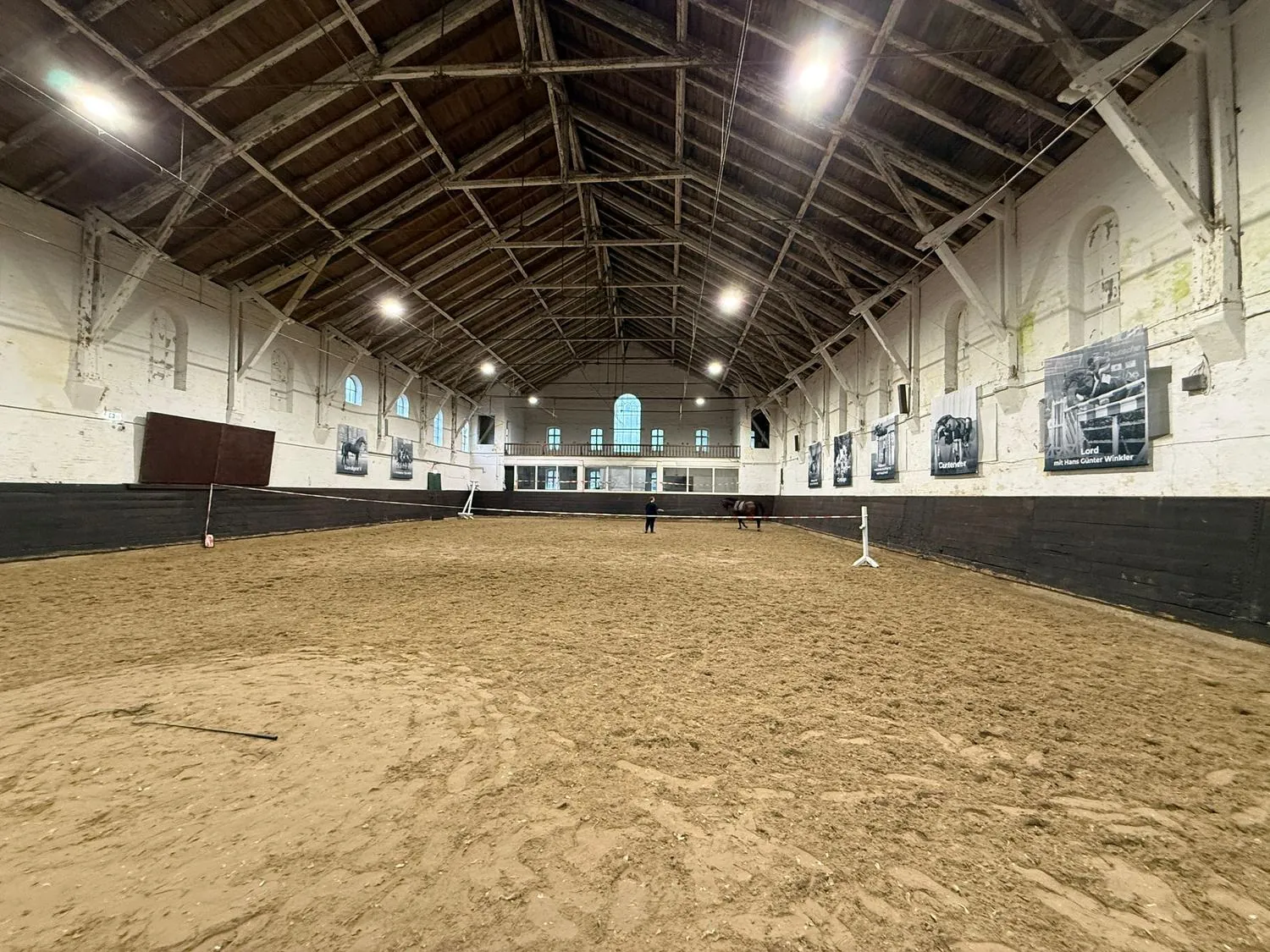 Alte Reithalle im Reitbetrieb mit Sandboden, Empore und historischen Pferdeportraits an den Wänden