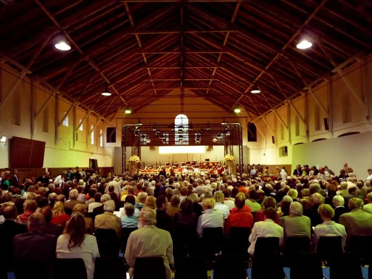Volle Alte Reithalle bei einem Konzert, Publikum auf Stuhlreihen vor der Bühne