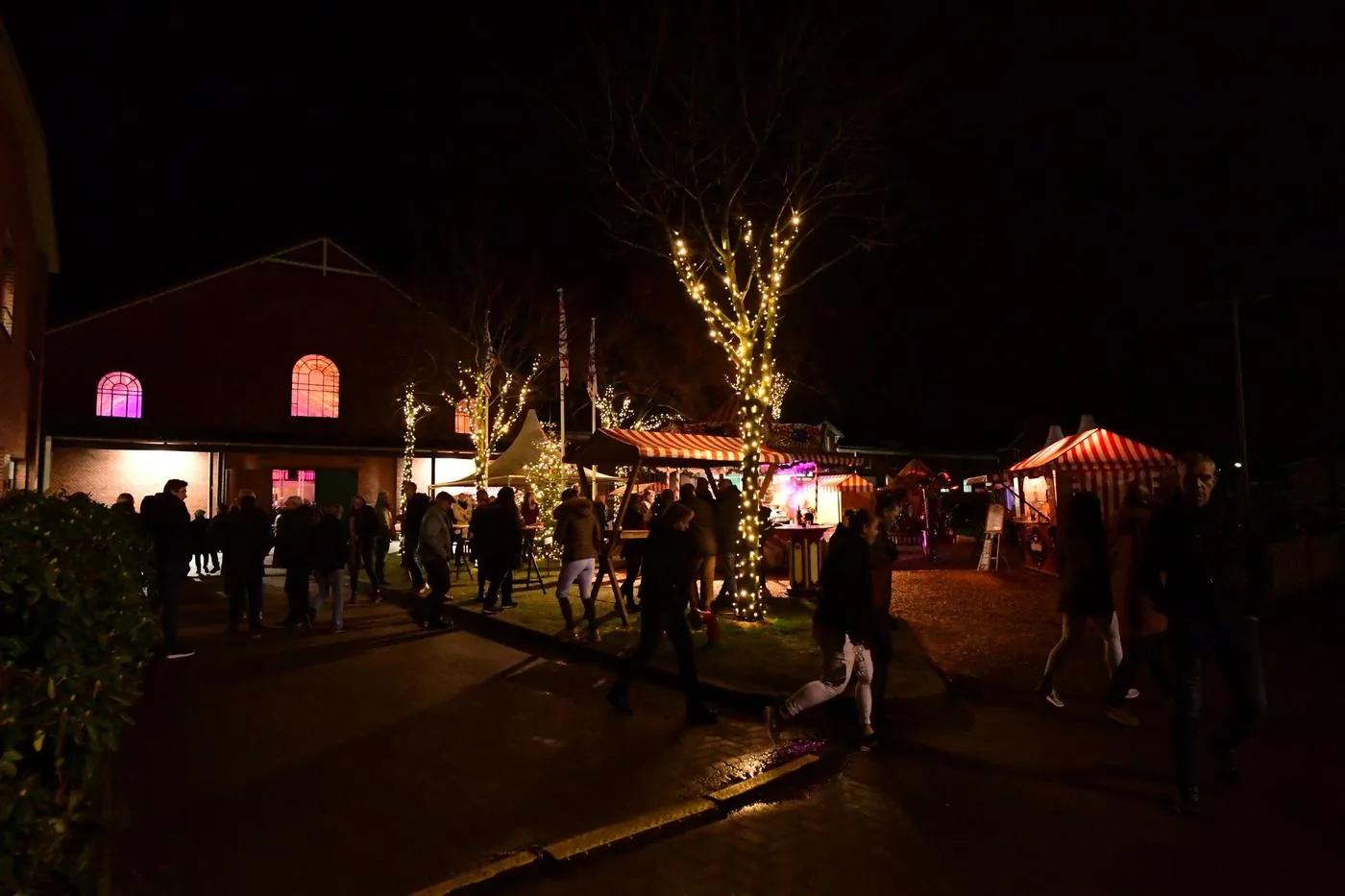 Beleuchtete Backsteinfassade der Reithalle bei Nacht mit Marktständen und Lichterketten davor