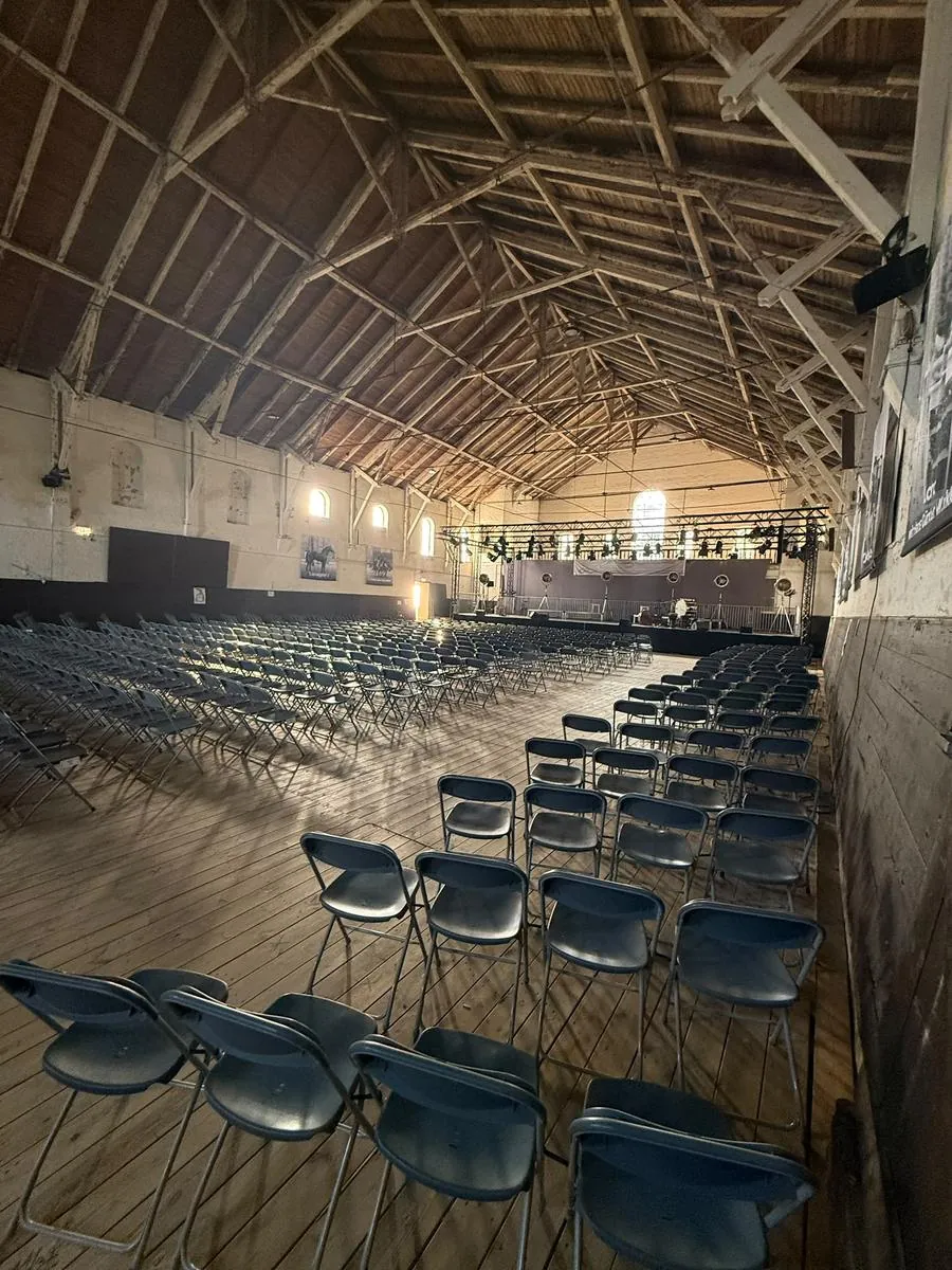 Alte Reithalle im Abendlicht mit Stuhlreihen und Bühne